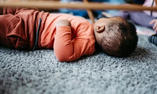 Kind liegt mit dem Rücken auf dem Boden