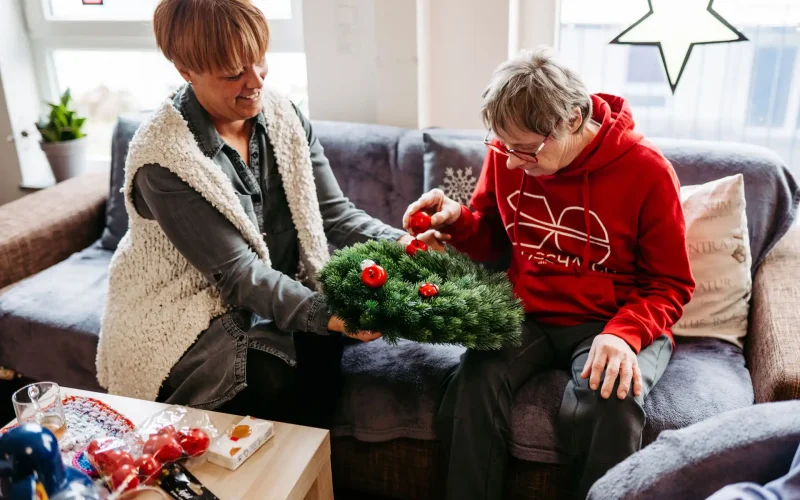 Lebenshelferin hilft Senioren beim Schmücken eines Kranzes