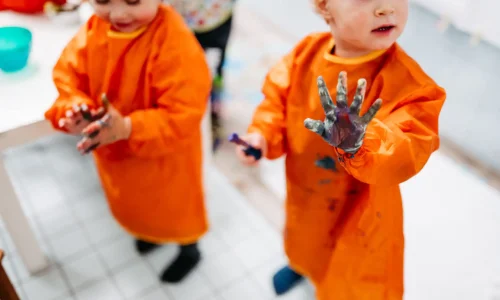 Zwei Kinder im orangenen Anzug beim malen mit Farbe